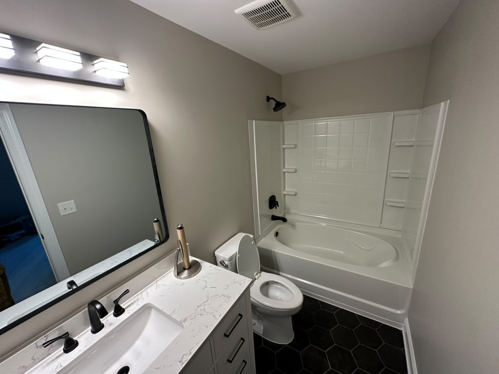 The same hall bathroom after the remodel, with a white tub surround, black hexagonal tile floor and a quartz-topped vanity