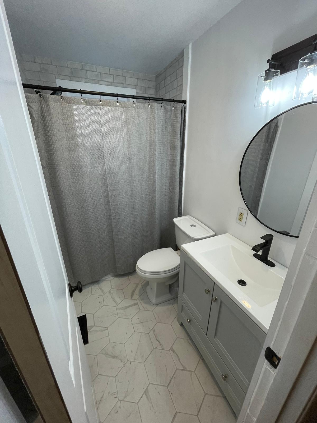 Guest bathroom gray vanity with round black-framed mirror