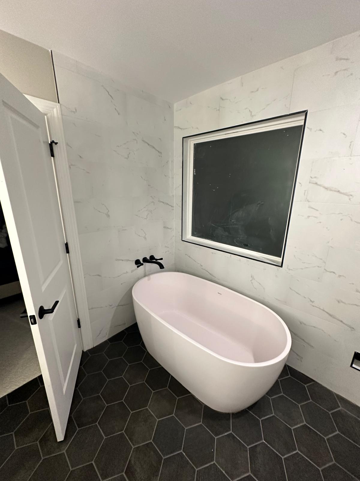 Master bathroom freestanding tub with large marble-look tile surround