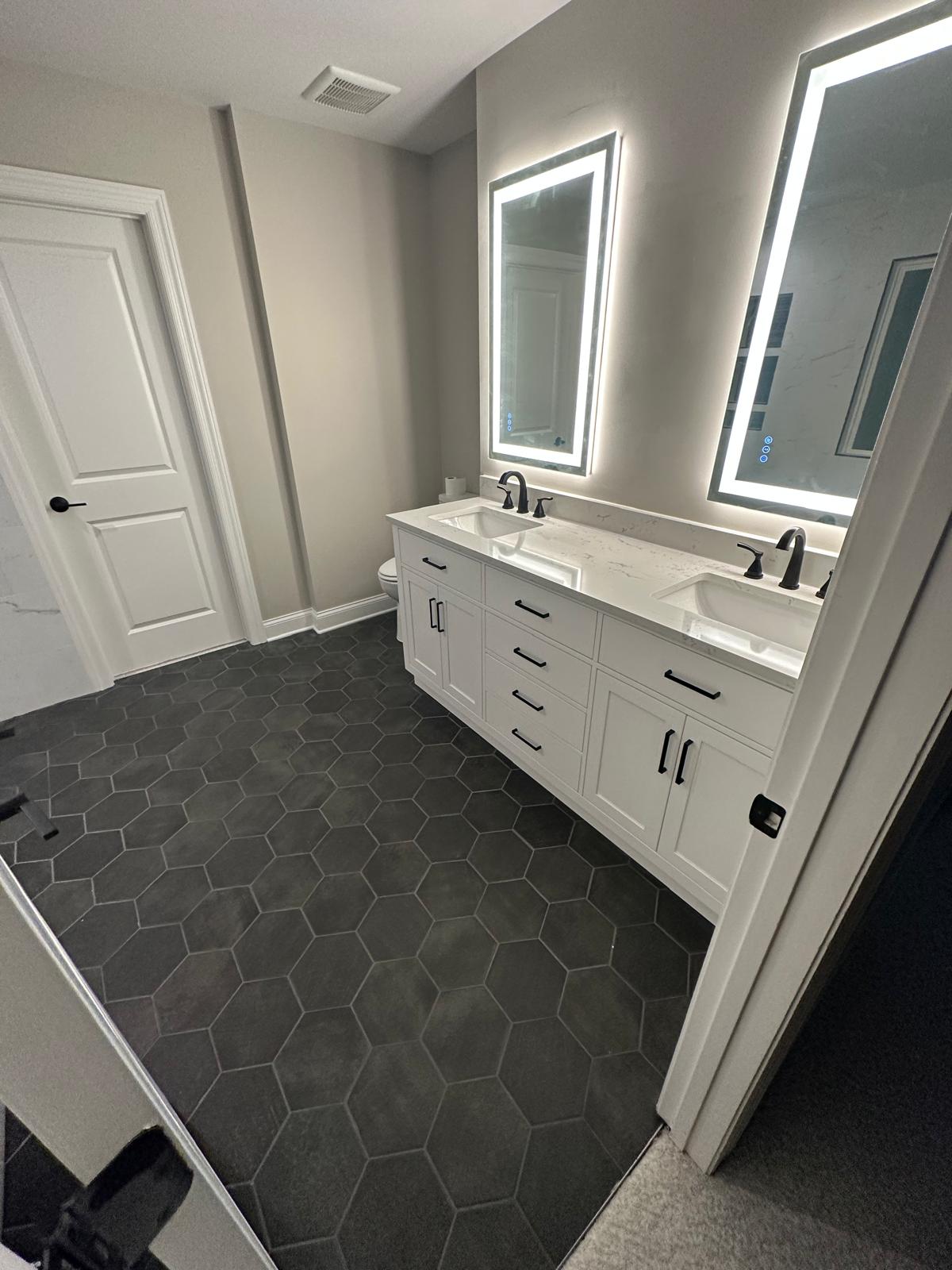 Master bathroom double vanity with LED mirrors and dark hexagonal tile floor