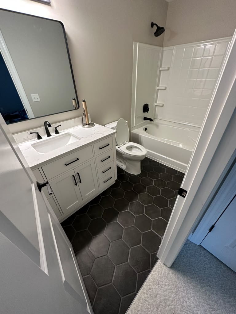 The same hall bathroom after the remodel, with a white vanity, quartz top, matte black fixtures and black hexagonal tile floor