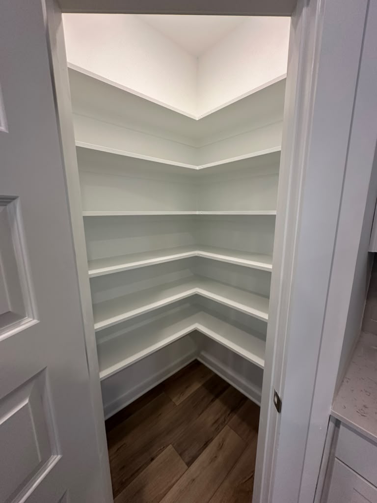 Pantry with white corner shelving over dark wood-look flooring