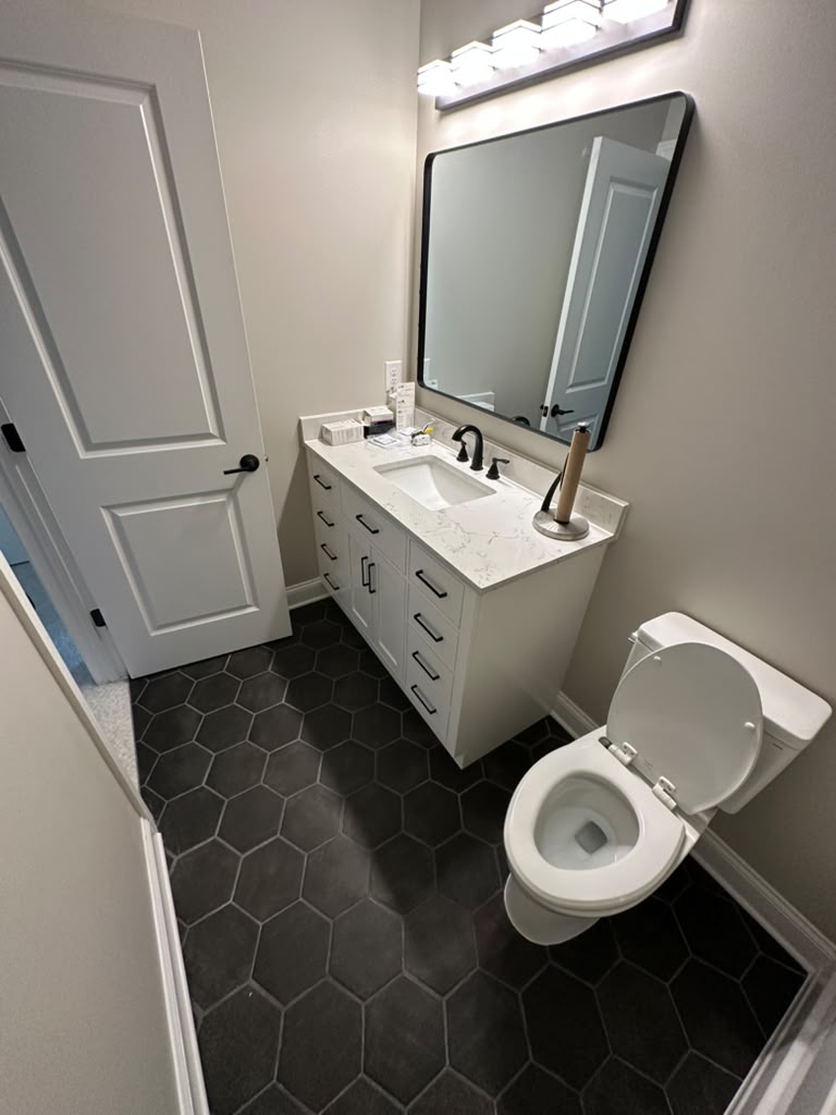 Powder room with a white shaker vanity, quartz top, matte black fixtures and black hexagonal tile floor