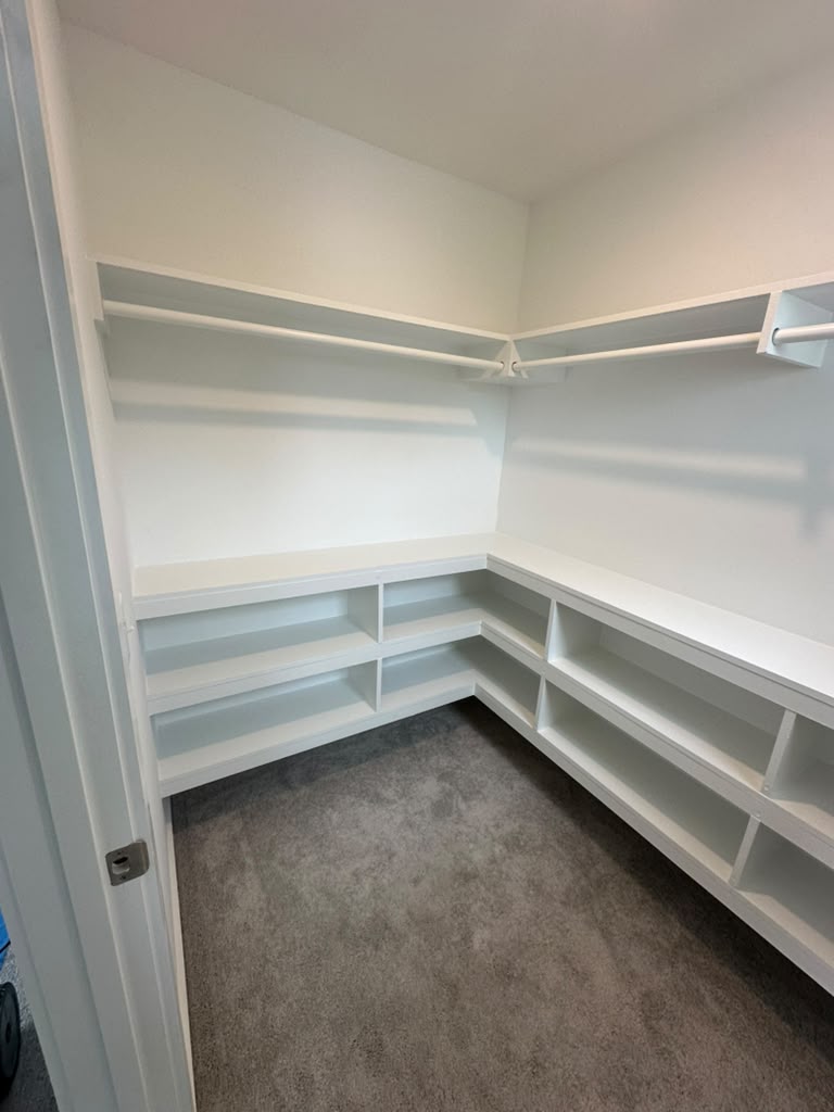 Walk-in closet with white corner shelving and hanging rods
